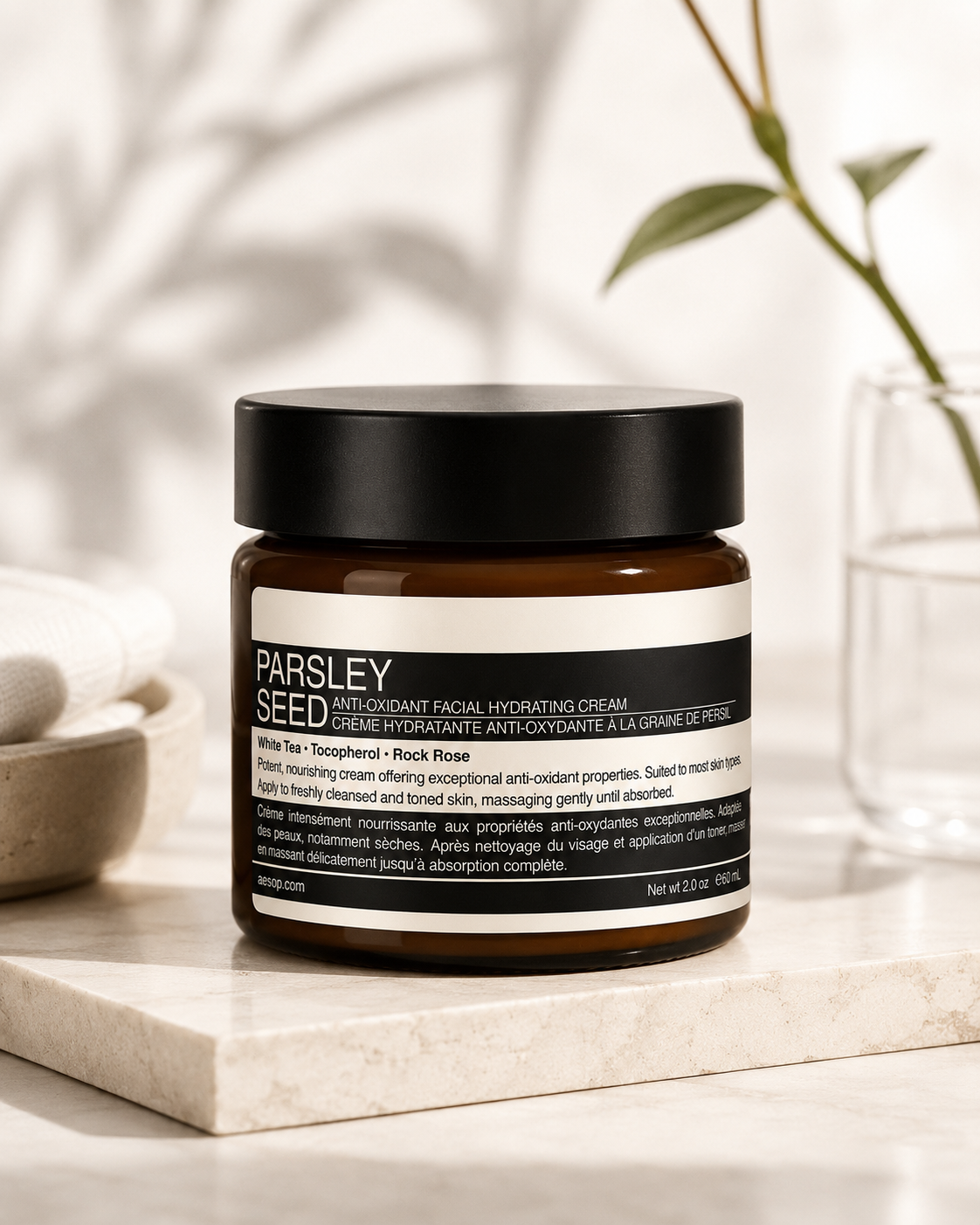 Aesop Parsley Seed Anti-Oxidant Facial Hydrating Cream displayed on a natural stone countertop in a bright, minimalist skincare setting with soft daylight, a folded towel, ceramic bowl, and glass vase with greenery. The calming spa-inspired composition highlights the antioxidant facial moisturizer as part of a premium daily skincare routine, emphasizing deep hydration, nourishment, and protection against environmental stressors.